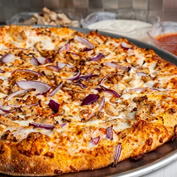 Chicken and red onion pizza on a metal tray with dipping sauces and chopped onions in the background.